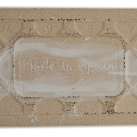 Um ladrilho retangular bege exibe o texto em relevo “Made in Spain” cercado por um padrão texturizado com os números 9, 5, 7 aci Um ladrilho retangular bege exibe o texto em relevo “Made in Spain” cercado por um padrão texturizado com os números 9, 5, 7 aci