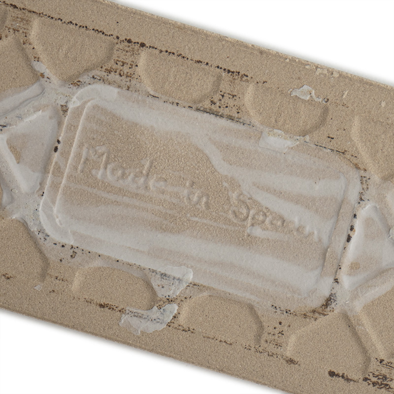 The beige ceramic tile features a raised geometric pattern. The embossed text `Made in Spain` is visible amidst the texture.