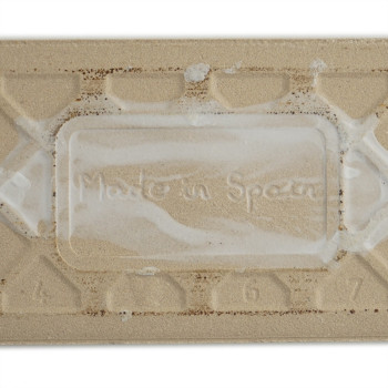 Eine rechteckige beige Fliese trägt in der Mitte den Aufdruck „Made in Spain“, umgeben von erhabenen geometrischen Mustern und d