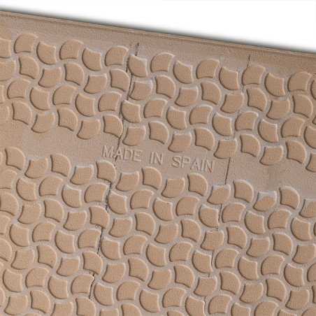 Op een lichtbruine tegel met een herhalend halfrond patroon en zichtbare scheuren staat in het midden de tekst `MADE IN SPAIN`.