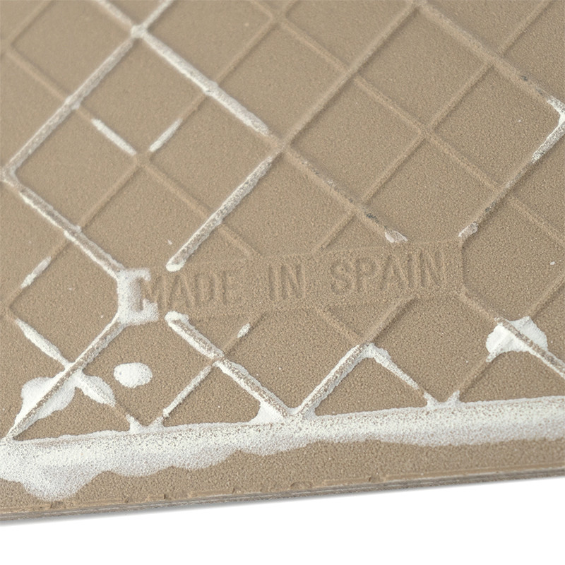 Azulejo cerâmico bege com padrão de grade com resíduo branco, exibindo o texto `MADE IN SPAIN` em relevo.
