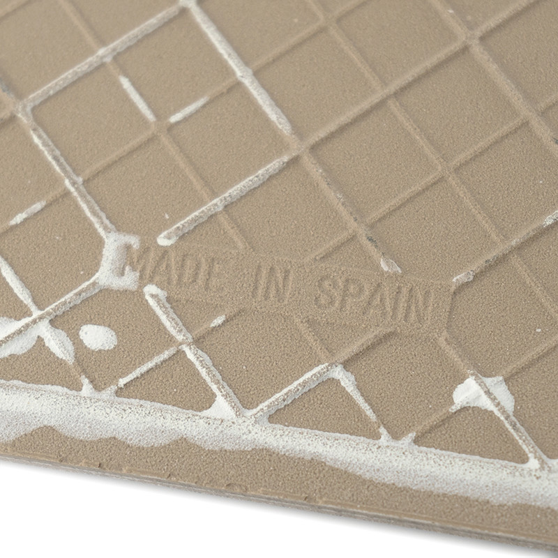 A beige tile features a geometric grid pattern with some white residue. Text reads `MADE IN SPAIN.`