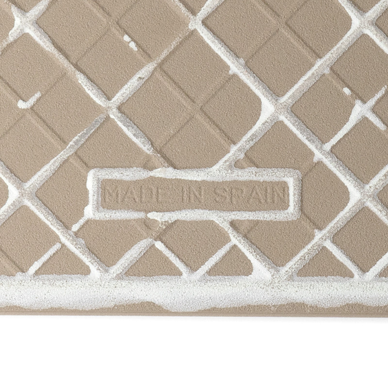 Un azulejo cerámico de color beige que presenta un patrón de cuadrícula con líneas diagonales que se cruzan. El texto dice `MADE