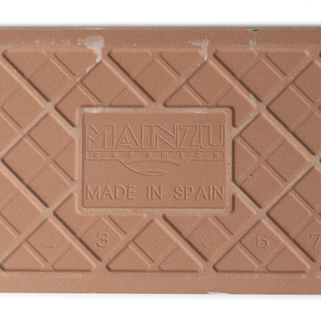 Eine strukturierte, braune Keramikfliese zeigt ein Gittermuster mit dem geprägten Text „MAINZU CERAMIC MADE IN SPAIN“ und den Za