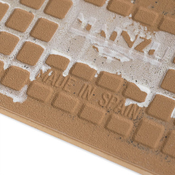 Le carreau marron présente une grille d'indentations carrées. Le texte blanc usé indique « MADE IN SPAIN », avec des marques de 