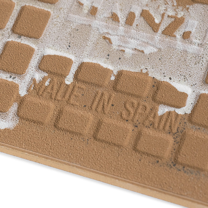 Een getextureerde keramische tegel heeft een rasterpatroon met licht verhoogde vierkanten. De tekst `MADE IN SPAIN` is in reliëf