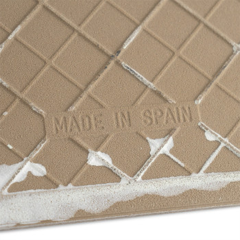 Un carreau de céramique texturé de couleur beige affiche le texte « MADE IN SPAIN » au milieu d'un motif en grille, avec un adhé