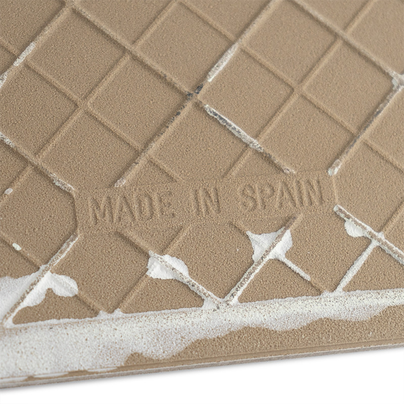 Eine hellbraune, strukturierte Keramikfliese trägt den Text „MADE IN SPAIN“ inmitten eines Gittermusters und ist an den Rändern 