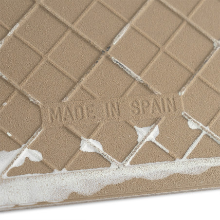 Un carreau de céramique texturé de couleur beige affiche le texte « MADE IN SPAIN » au milieu d'un motif en grille, avec un adhé