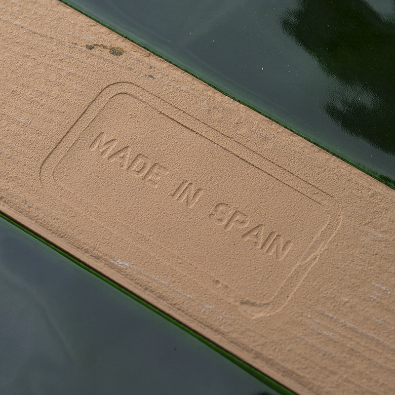 Um ladrilho cerâmico apresenta o texto em relevo `MADE IN SPAIN.` O ladrilho combina o verde brilhante com uma superfície textur