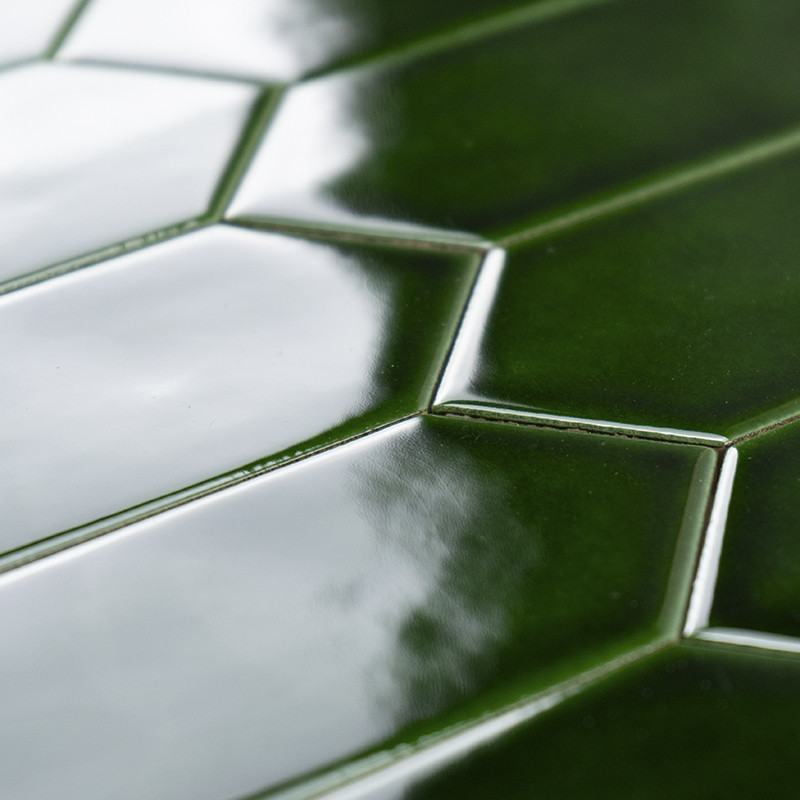 Los azulejos de cerámica de color verde brillante forman un patrón en espiga que refleja la luz en un ambiente interior luminoso
