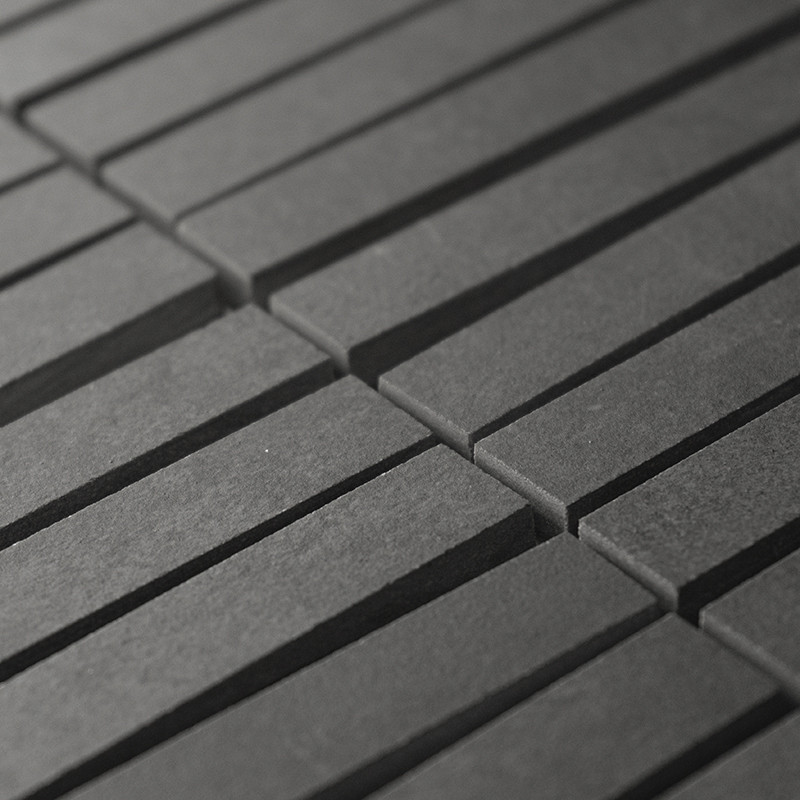 Ladrilhos retangulares cinza escuro se alinham em fileiras paralelas, criando um padrão rítmico. Os ladrilhos formam uma superfí
