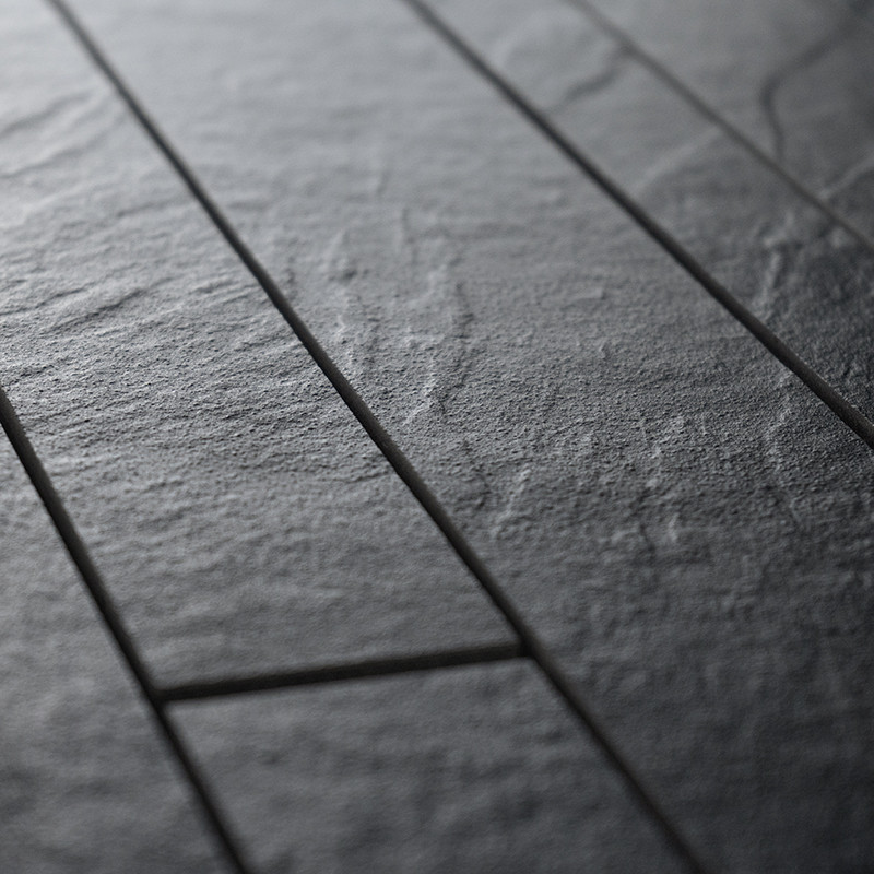 Rectangular, textured tiles with a rough, stone-like surface form an organized pattern. They are placed closely together, creati