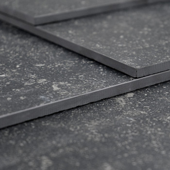 Drie overlappende donkergrijze tegels, rustend op een gestructureerd oppervlak, vertonen een gespikkeld patroon met licht opstaa