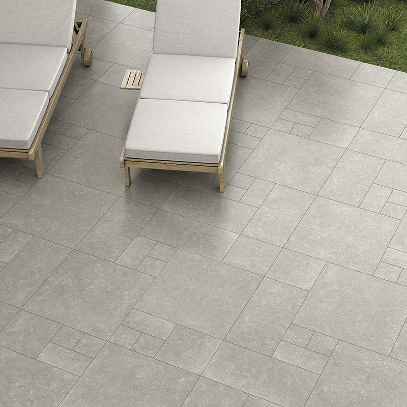 Des carreaux de pierre grise forment un motif géométrique sur un patio avec deux chaises longues rembourrées à proximité, entour