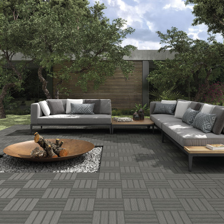 Twee grijze banken omlijsten een modern buitenterras met in elkaar grijpende tegels. Een centrale vuurplaats op grind versterkt 