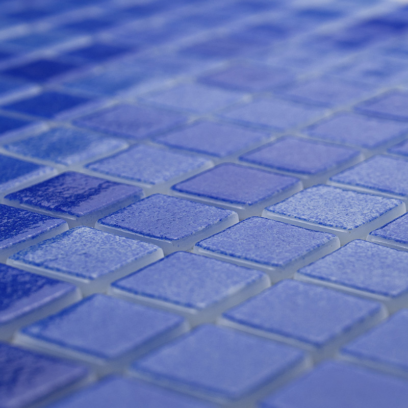 Ladrilhos de vidro azul formam um padrão de mosaico texturizado, criando uma superfície cintilante em um espaço suavemente ilumi