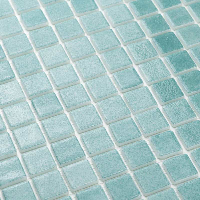 Les carreaux de verre turquoise sont soigneusement disposés selon un motif en grille, créant une surface texturée et réfléchissa
