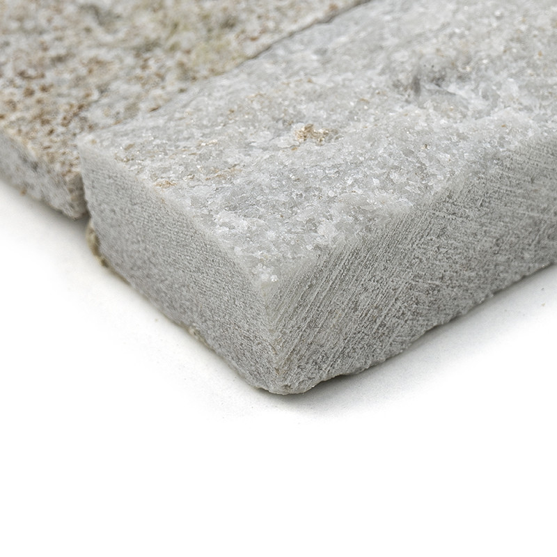 Ladrilhos de pedra áspera e texturizada ficam empilhados horizontalmente, apresentando uma mistura natural e terrosa de tons cla