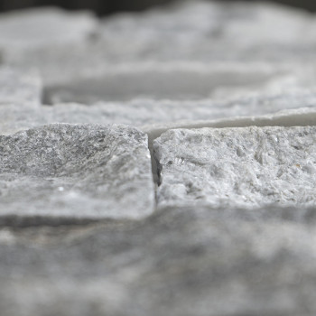 Rough-textured stone tiles lie in a staggered arrangement, creating a natural, uneven surface in a neutral setting.