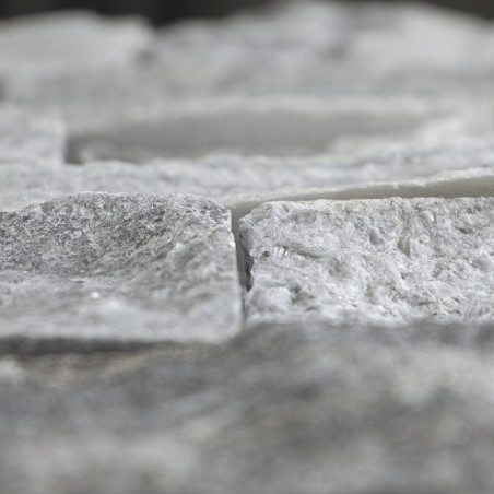 Rough-textured stone tiles lie in a staggered arrangement, creating a natural, uneven surface in a neutral setting.