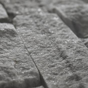 Rough, rectangular stone tiles reflect light, creating a sparkling effect in a close-up view, laid in an interlocking pattern.