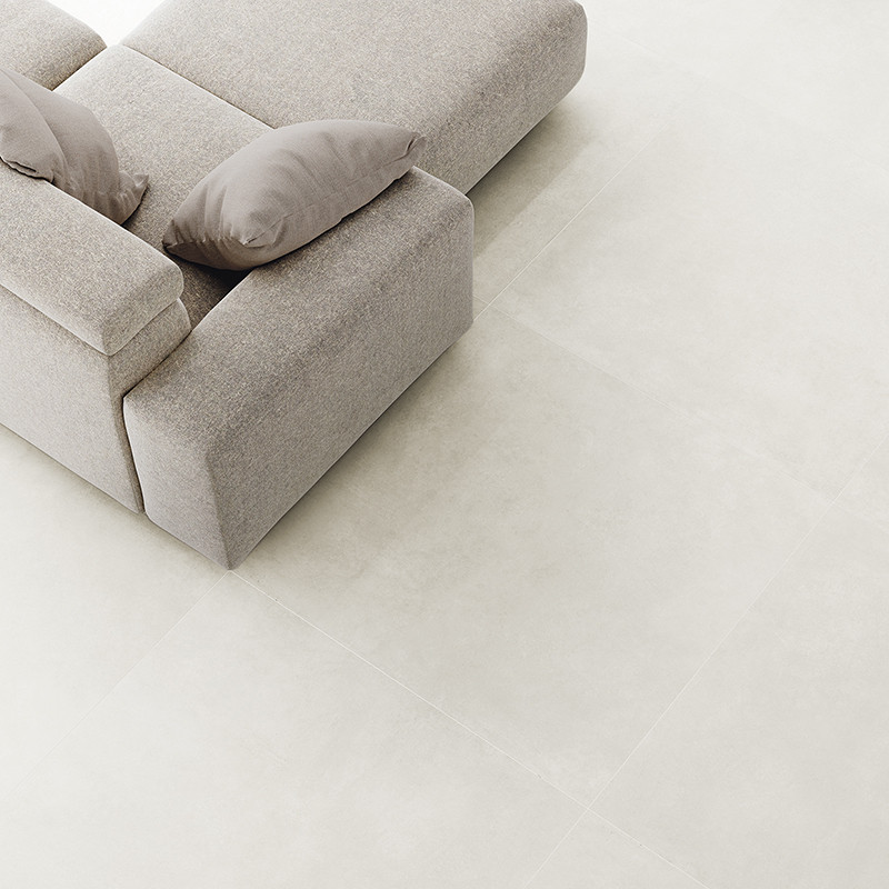 Um sofá cinza-claro texturizado com duas almofadas sobre um chão de grandes azulejos claros Um sofá cinza-claro texturizado com duas almofadas sobre um chão de grandes azulejos claros
