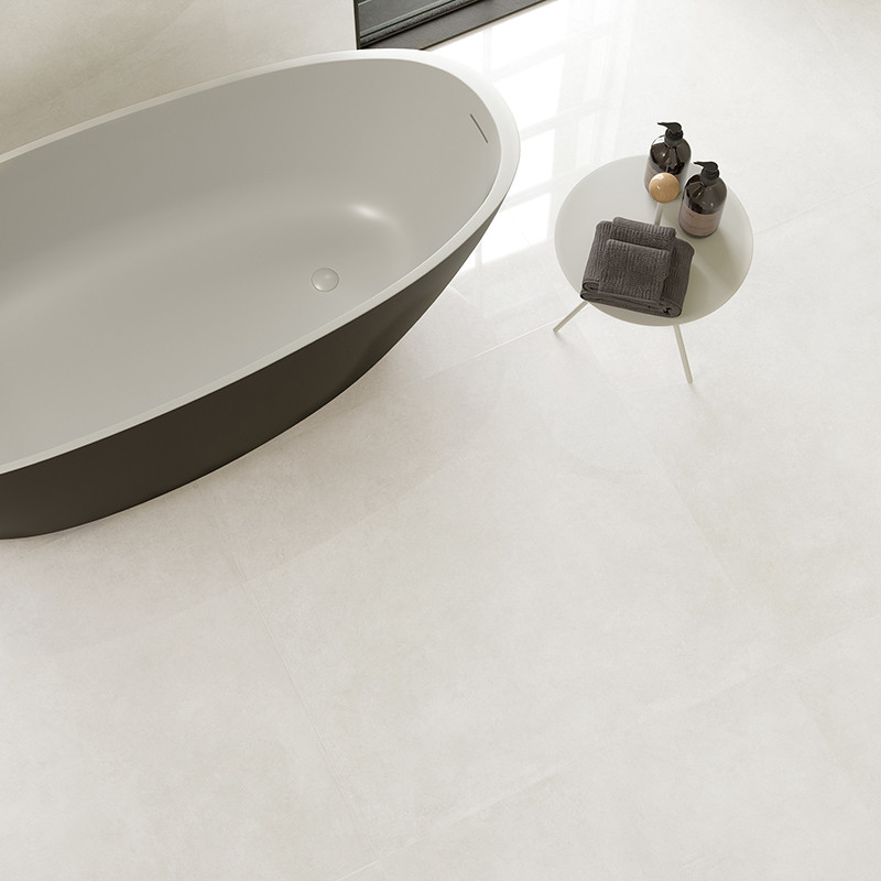 Eine moderne, ovale Badewanne steht neben einem runden, weißen Tisch mit Toilettenartikeln in einem minimalistischen Badezimmer 