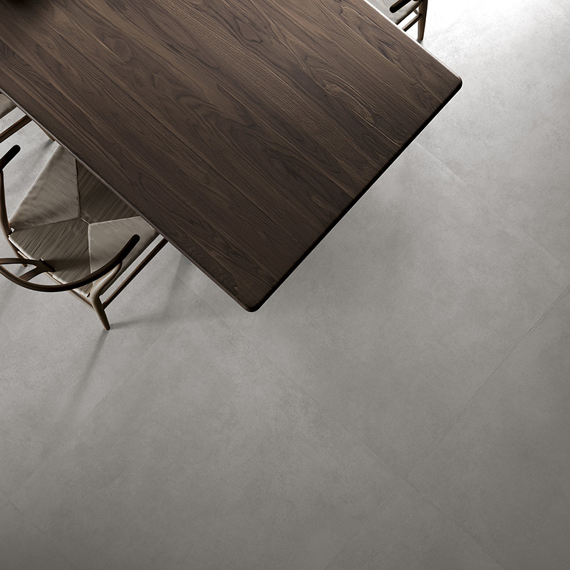 Una mesa de madera oscura se asienta sobre un piso de azulejos lisas de color gris claro, rodeada de sillas de tela beige, crean