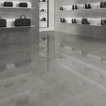 Der graue Fliesenboden glänzt und spiegelt ein Einzelhandelsumfeld mit Regalen mit dunklen Ledertaschen und Stiefeln vor grauen 