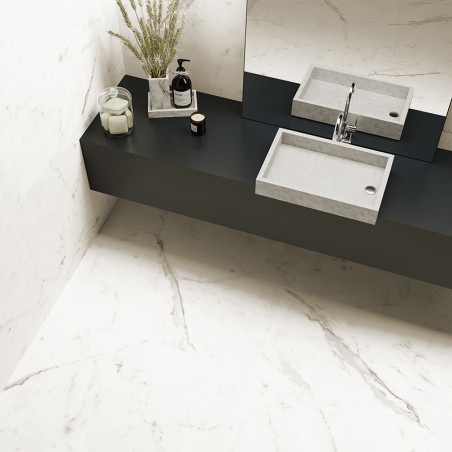 A rectangular concrete sink sits atop a black counter in a bathroom, decorated with a vase, bottle, and candles, surrounded by m