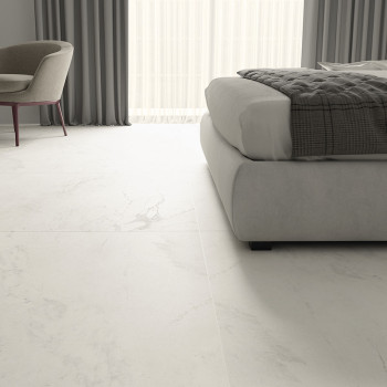 O piso de mármore branco se estende por um quarto moderno, com cadeira e cama almofadadas, com cortinas cinza emoldurando uma gr