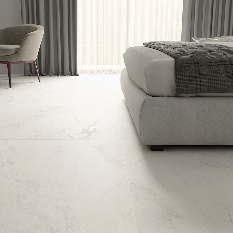 O piso de mármore branco se estende por um quarto moderno, com cadeira e cama almofadadas, com cortinas cinza emoldurando uma gr