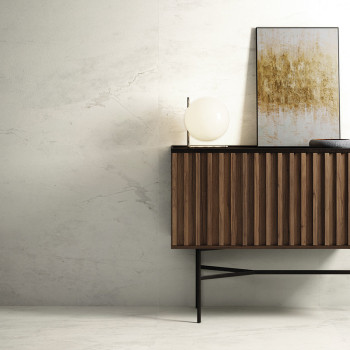 Un buffet en bois se dresse contre un mur aux motifs de marbre clair. Une lampe sphérique et des œuvres d’art abstraites reposen