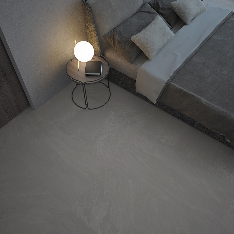 A smooth, gray tile floor lies adjacent to a modern bed. a round side table with a glowing lamp rests nearby.