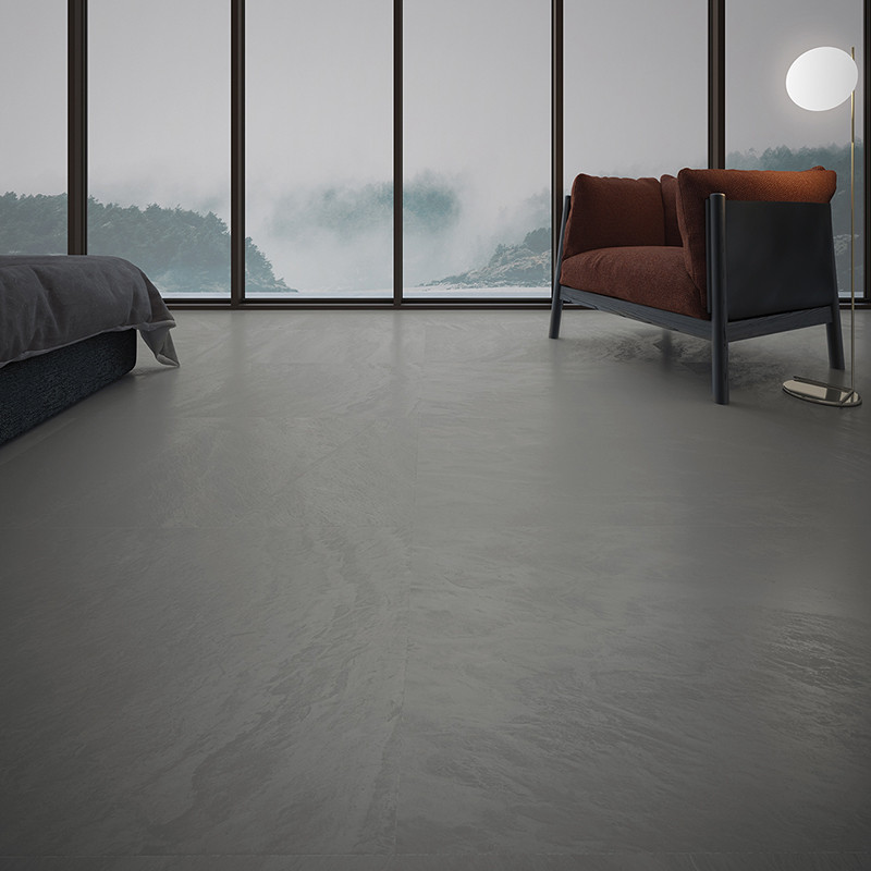 A smooth, gray tile floor supports a modern room with a brown armchair, a nearby bed, and large windows revealing a misty landsc