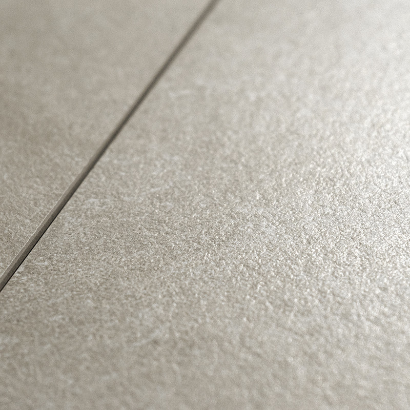 A textured, matte ceramic tile sits in close-up view, showcasing its subtle, light gray surface. A visible grout line divides th