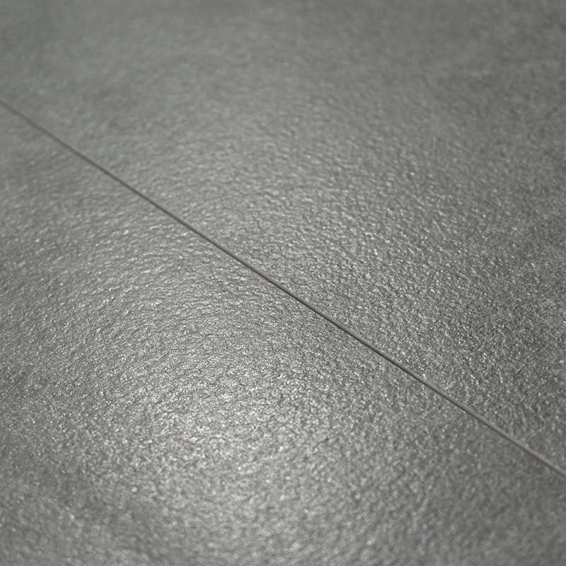 O piso com textura cinza, mostrando um brilho sutil, fica plano. Uma linha estreita de argamassa divide os ladrilhos, sugerindo 
