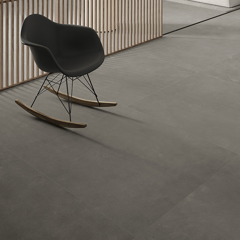 Een strakke, zwarte schommelstoel rust op grote, gladde grijze tegels in een modern interieur met houten lattenbodem.