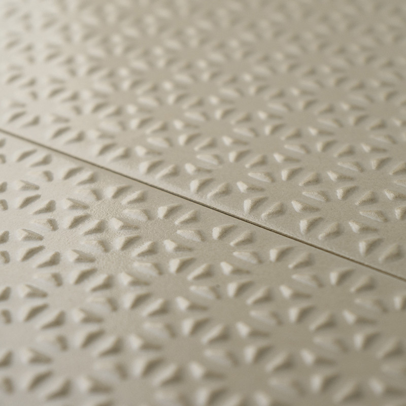 Los azulejos beige presentan un patrón floral en relieve que se repite, creando textura y profundidad. Los azulejos se alinean e
