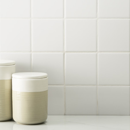 Dois potes de cerâmica de cor creme estão apoiados sobre uma superfície lisa contra um fundo de azulejos brancos uniformes.