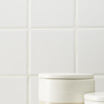 Dois potes de cerâmica branca com tampas assentam sobre um fundo de azulejos quadrados brancos e lisos com linhas de argamassa v