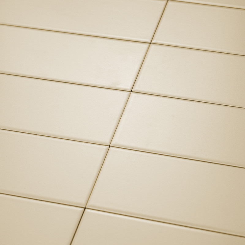 Ladrilhos retangulares de cor creme estão bem organizados em um padrão de grade diagonal. A superfície lisa reflete a luz unifor