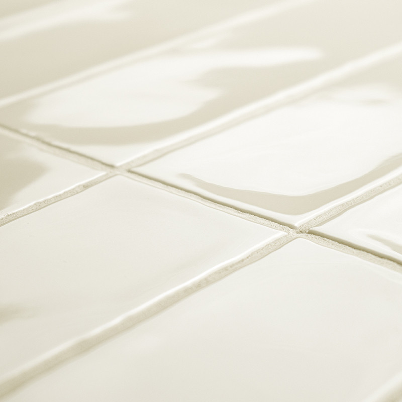 Glossy white rectangular tiles form a grid pattern, reflecting light in a spacious room, with slightly visible grout lines.