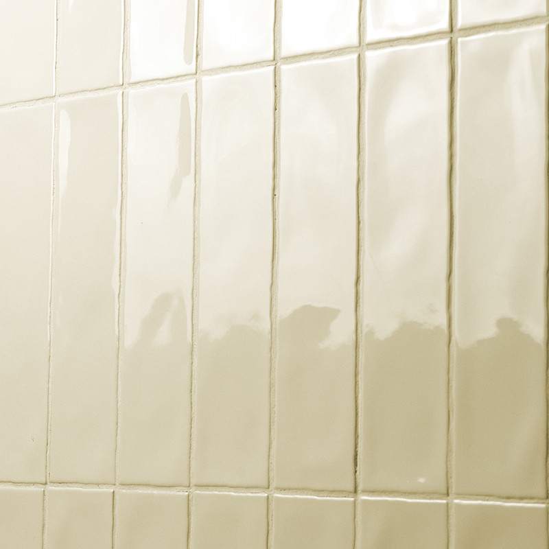 Rectangular, glossy tiles are arranged in a grid pattern on a wall, reflecting light in a bathroom or kitchen.