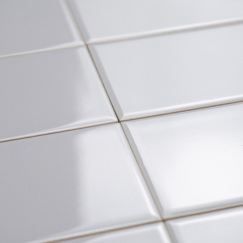 Ladrilhos cerâmicos brancos e brilhantes ficam planos, refletindo a luz sutilmente. Eles estão dispostos em um padrão de grade, 