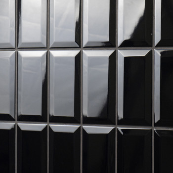 Glänzend schwarze rechteckige Fliesen sind in einem Gittermuster angeordnet. Sie reflektieren das Licht und verleihen einer Wand