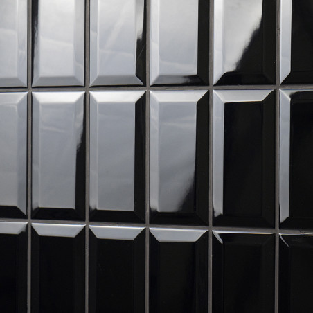 Glänzend schwarze rechteckige Fliesen sind in einem Gittermuster angeordnet. Sie reflektieren das Licht und verleihen einer Wand