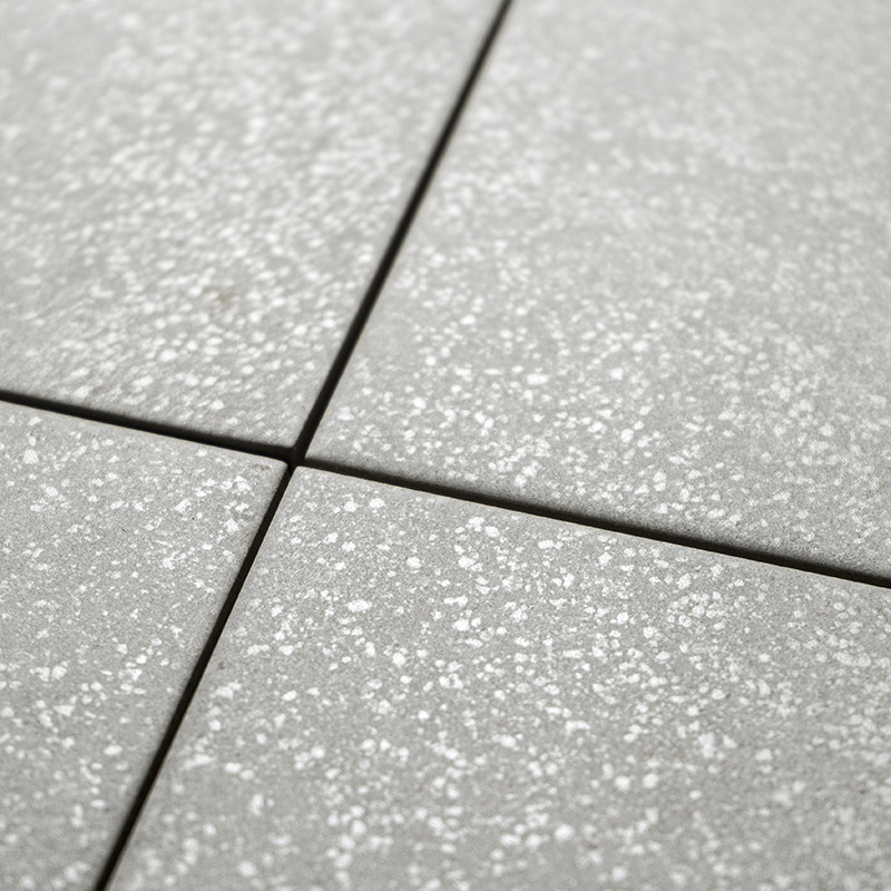 Les carreaux carrés gris affichent un subtil motif moucheté, créant une surface texturée. Ils sont disposés en grille, formant u