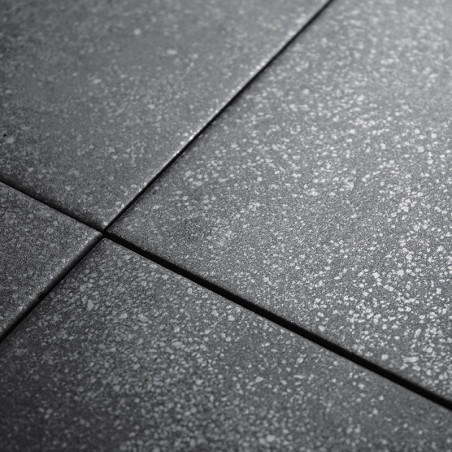 Vier dunkelgraue Fliesen weisen eine dezent gesprenkelte Textur auf. Sie sind eng aneinandergereiht und bilden bei künstlicher B
